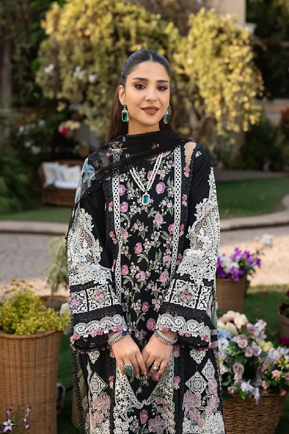 "Full view of a model wearing a black floral embroidered suit with emerald jewelry and pearl accents."